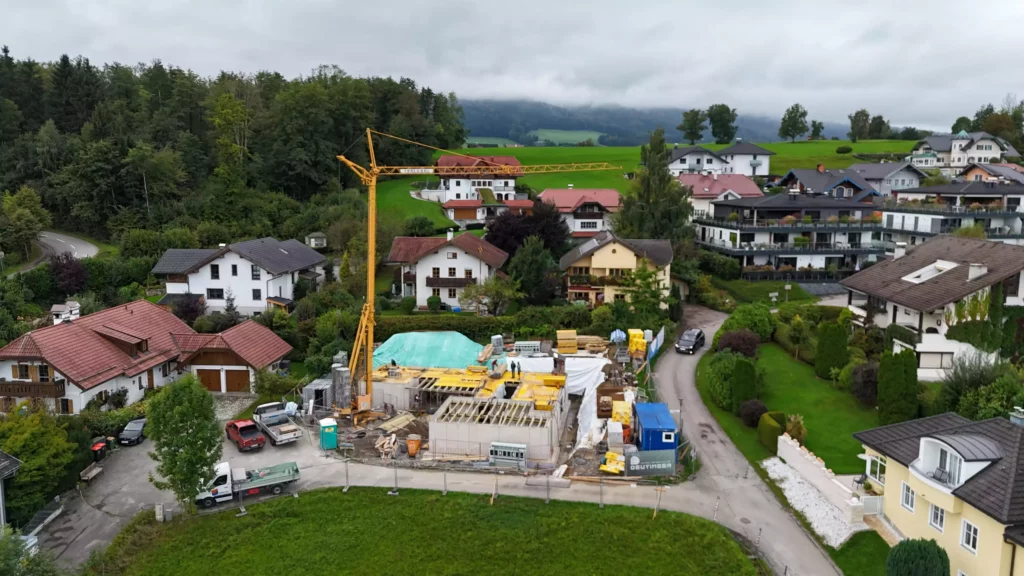 default Bauprojekt mit Kran und Baustelle in einem Wohngebiet mit Einfamilienhäusern und viel Grün im Hintergrund bei bewölktem