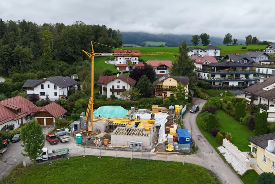 Bauprojekt mit Kran und Baustelle in einem Wohngebiet mit Einfamilienhäusern und viel Grün im Hintergrund bei bewölktem