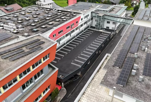 Luftaufnahme eines modernen Bürogebäudes mit roten Fassaden und zahlreichen Solarpaneelen auf den Dächern im Bereich