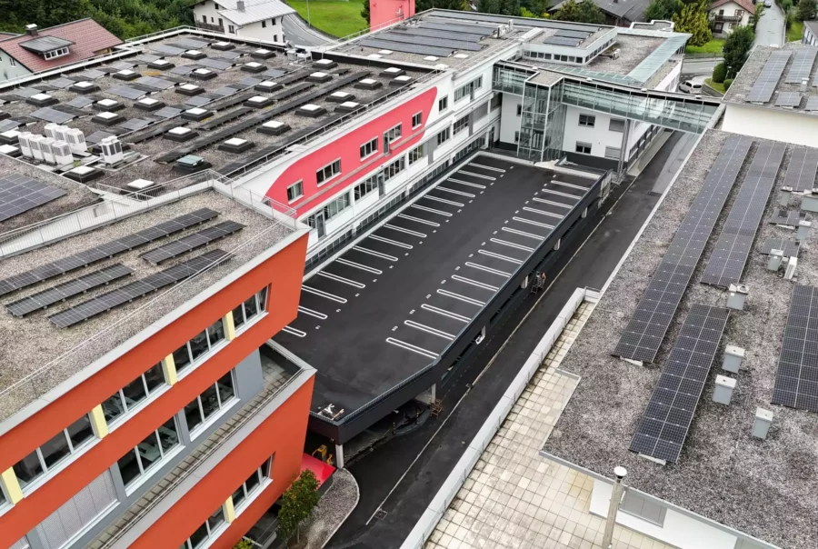 Luftaufnahme eines modernen Bürogebäudes mit roten Fassaden und zahlreichen Solarpaneelen auf den Dächern im Bereich