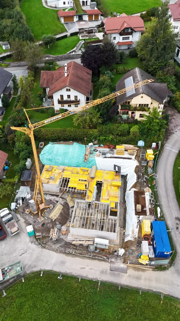 default Baustelle mit Baukran und Rohbau eines Gebäudes in einem Wohngebiet mit angrenzenden Einfamilienhäusern und viel Grünfläche