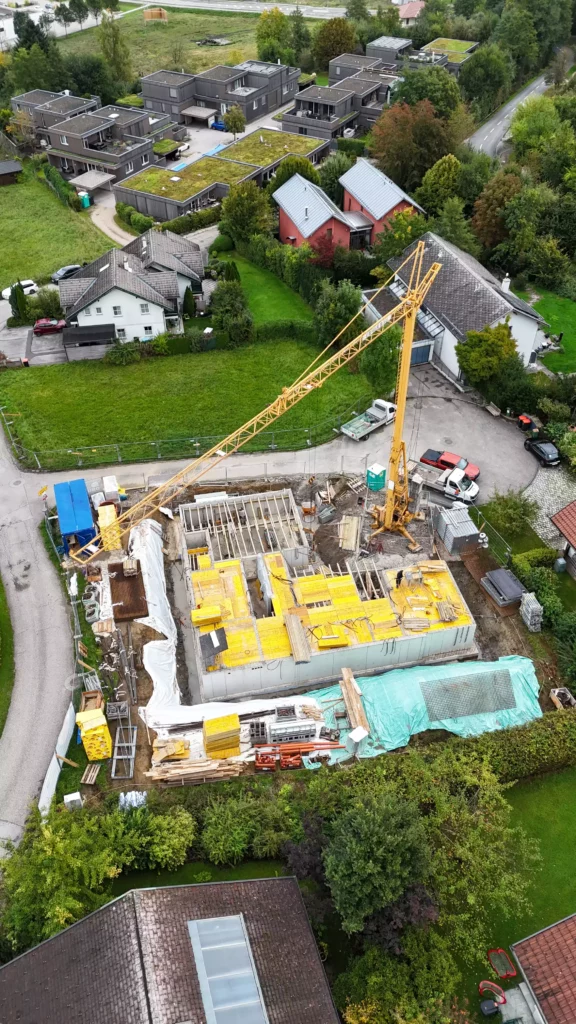 default Baustelle mit gelbem Baukran und Rohbau in einem Wohngebiet mit Einfamilienhäusern und moderner Wohnbebauung umgeben von