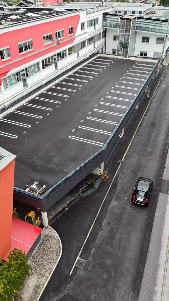 default Leeres Parkdeck neben einem modernen Bürogebäude mit rotem Fassadenelement und einem schwarzen Auto auf der Straße darunter