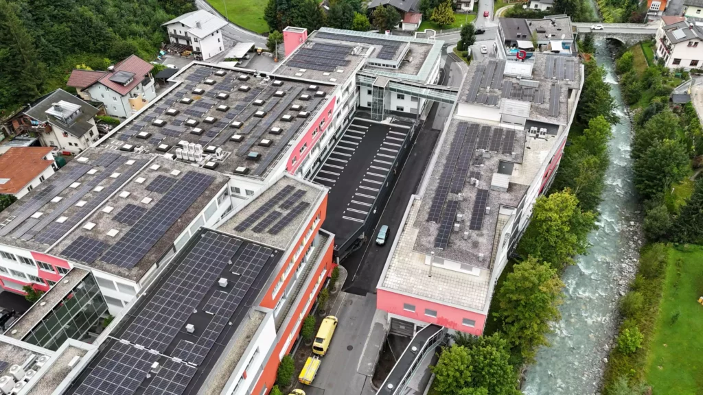 06_eurofunk Luftaufnahme eines großen Gebäudekomplexes mit Solaranlagen auf den Dächern neben einem Fluss und umgeben von Bäumen und