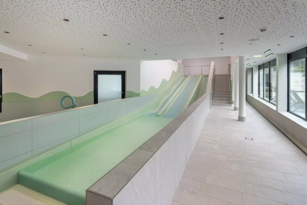 2024-06-13_Deutinger-Hotel-Kesselgrub-©sobietzki-high-res-11 Innenansicht eines modernen Hallenbads mit Wasserrutsche und Treppe im Hotel Kesselgrub, Deutinger Projektentwicklung.