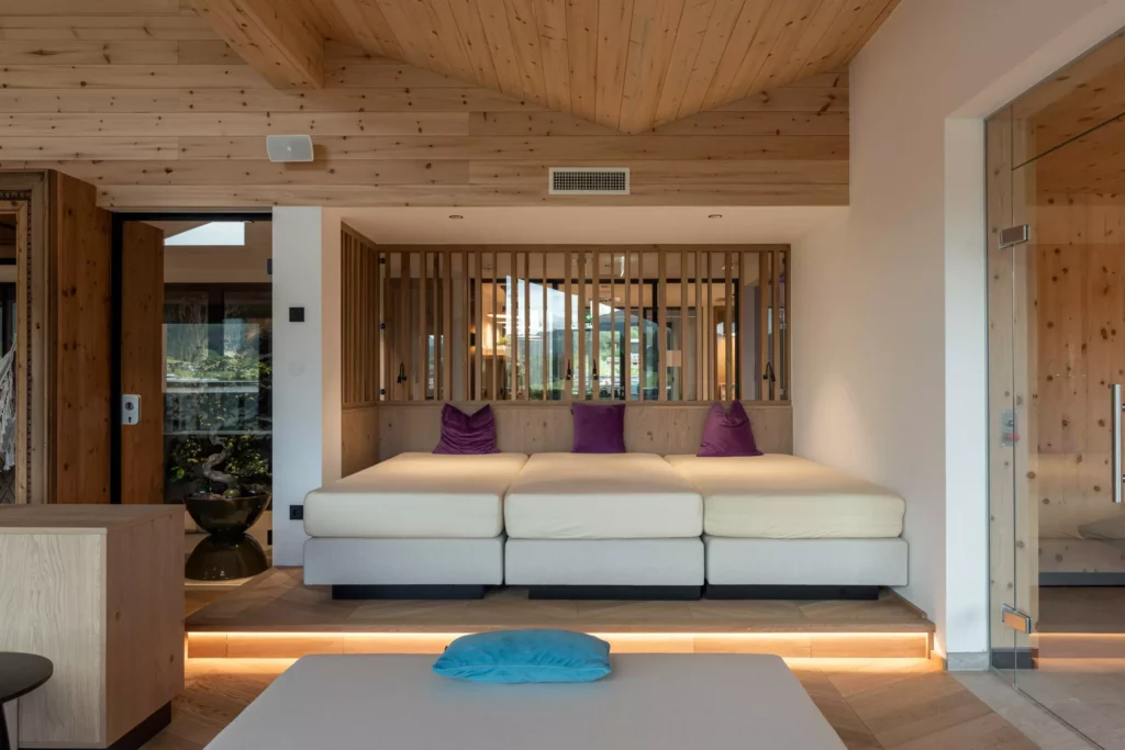 2024-06-13_Deutinger-Hotel-Kesselgrub-©sobietzki-high-res-22 Modern eingerichteter Hotel-Loungebereich mit hellen Sitzpolstern, lila Kissen und Holzverkleidung im Deutinger Hotel
