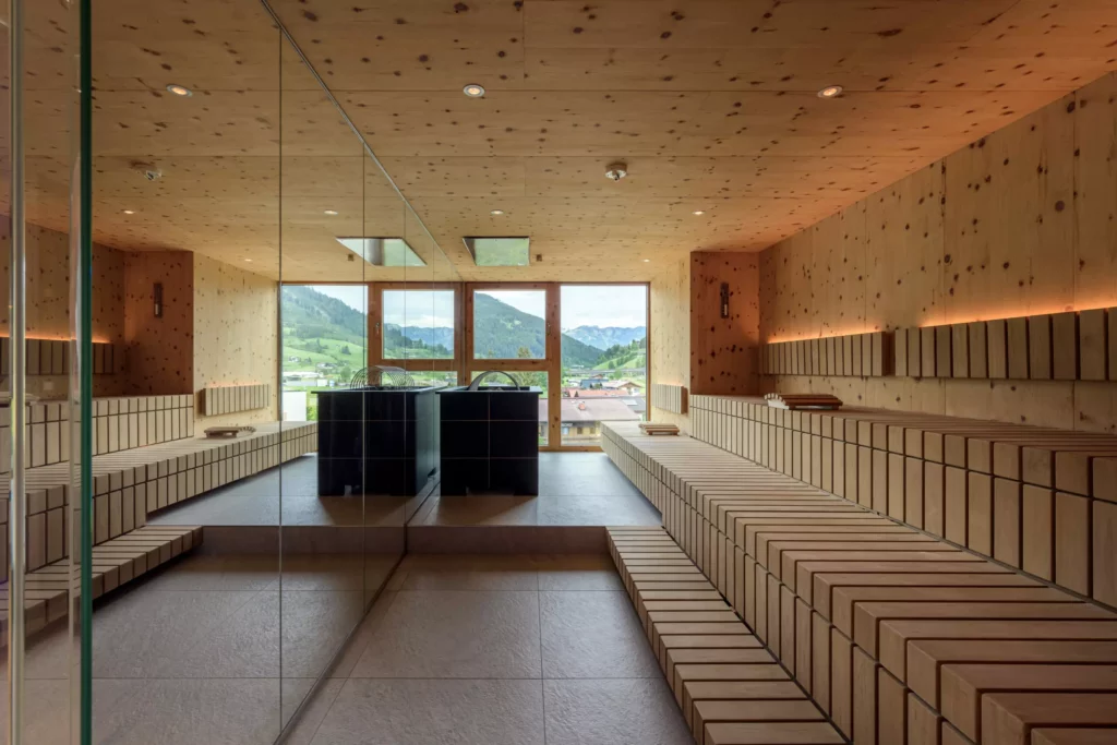 2024-06-13_Deutinger-Hotel-Kesselgrub-©sobietzki-high-res-24 Moderne Sauna mit Holzverkleidung, großen Fenstern und Blick auf grüne Berge und Dorf im Deutinger Hotel Kesselgrub