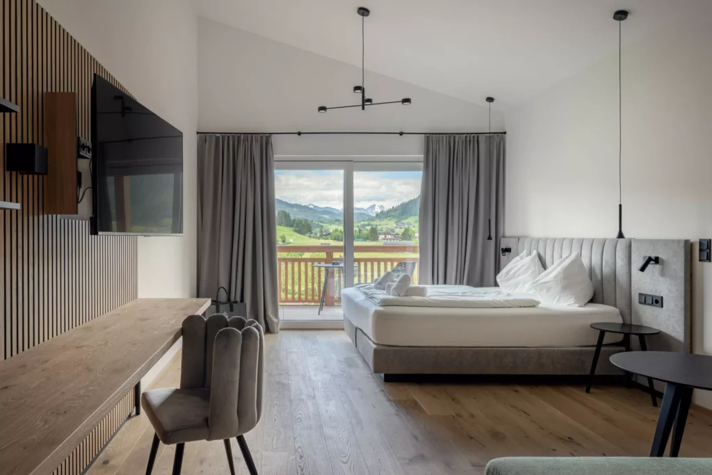 2024-06-13_Deutinger-Hotel-Kesselgrub-©sobietzki-high-res-31 Modern eingerichtetes Hotelzimmer mit Doppelbett, Schreibtisch, TV und Balkon mit Bergblick im Deutinger Hotel Kesselgrub