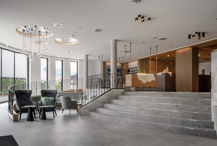 Moderne Hotellobby mit Sitzgruppen, großen Fenstern, Treppe und Holz-Elementen im Deutinger Hotel Kesselgrub Innenbereich.