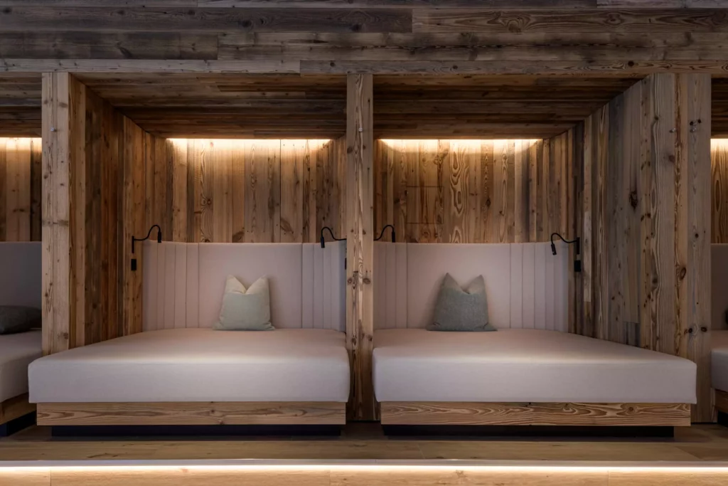 2024-06-13_Deutinger-Hotel-Kesselgrub-©sobietzki-high-res-5 Zwei moderne Lounge-Betten mit beigen Polstern und Kissen in einer Holzvertäfelten Nische mit indirekter Beleuchtung