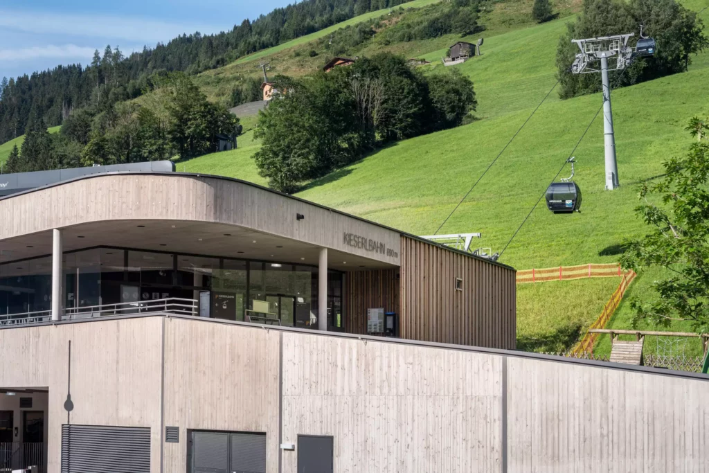 2024-08-19_Talstation-Kieserl-Grossarl-©sobietzki-low-res-2560px-13 Moderne Talstation der Kieserlbahn in Großarl vor grünen Almwiesen mit Gondelbahn und bewaldetem Berg im Hintergrund