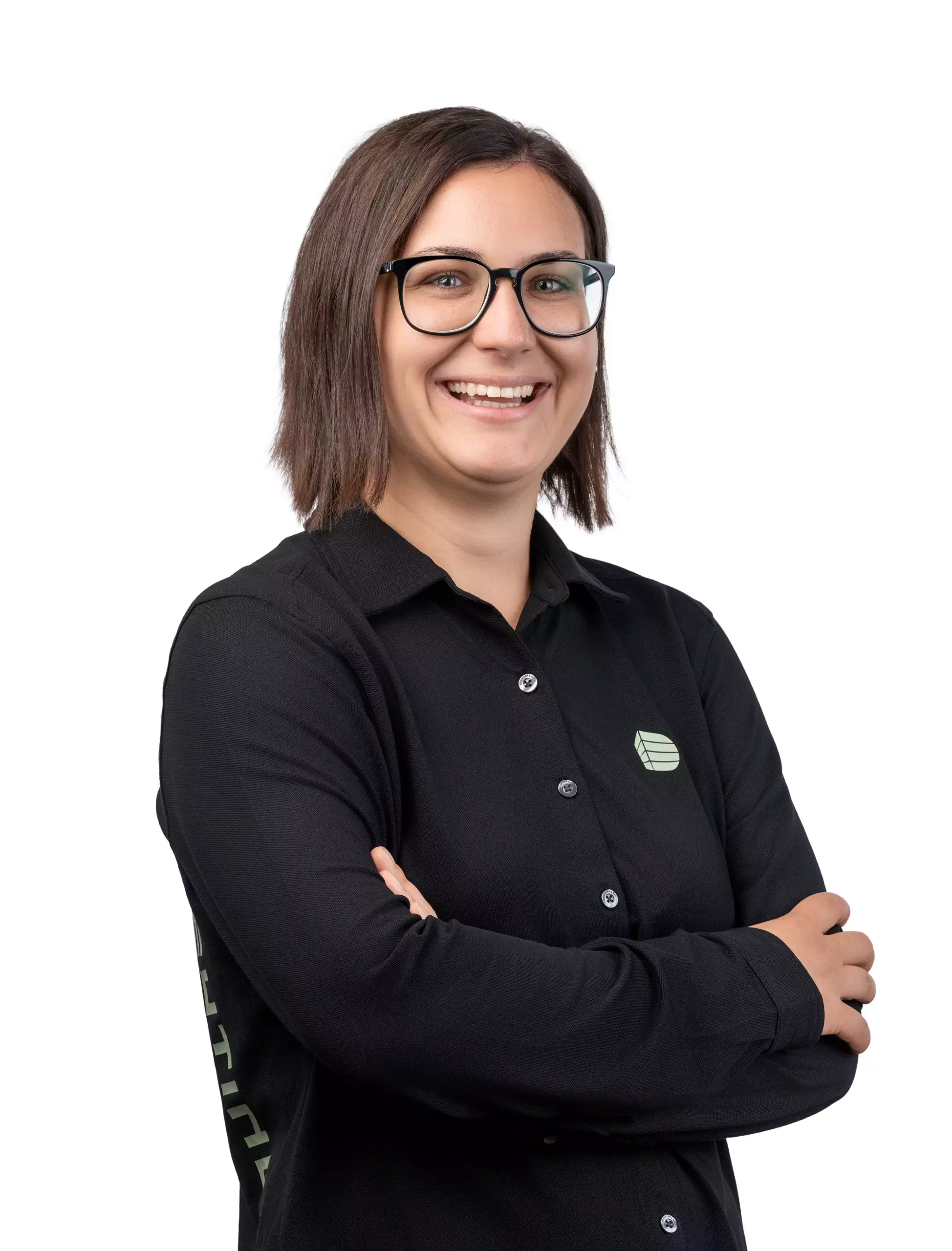 Junge Frau mit Brille und schwarzem Hemd mit Logo lächelt mit verschränkten Armen vor weißem Hintergrund