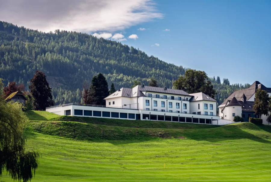 Modernes weißes Mitarbeiterhaus vor bewaldetem Berghang und grünem Wiesengelände bei Pichlarn unter blauem Himmel