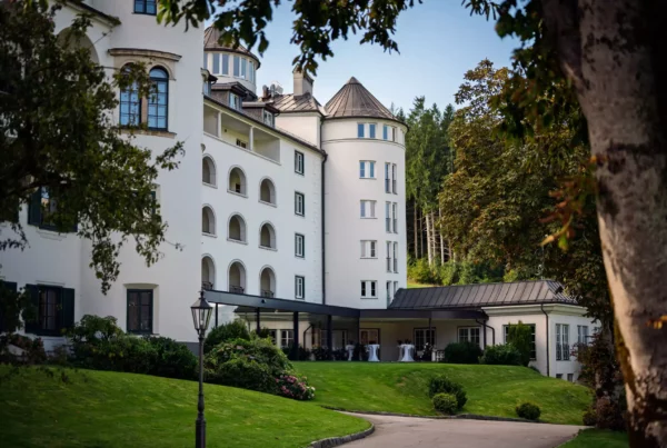 Weißes historisches Gebäude mit Rundturm, Arkaden und gepflegtem Garten in Pichlarn, umgeben von Bäumen und Wald im