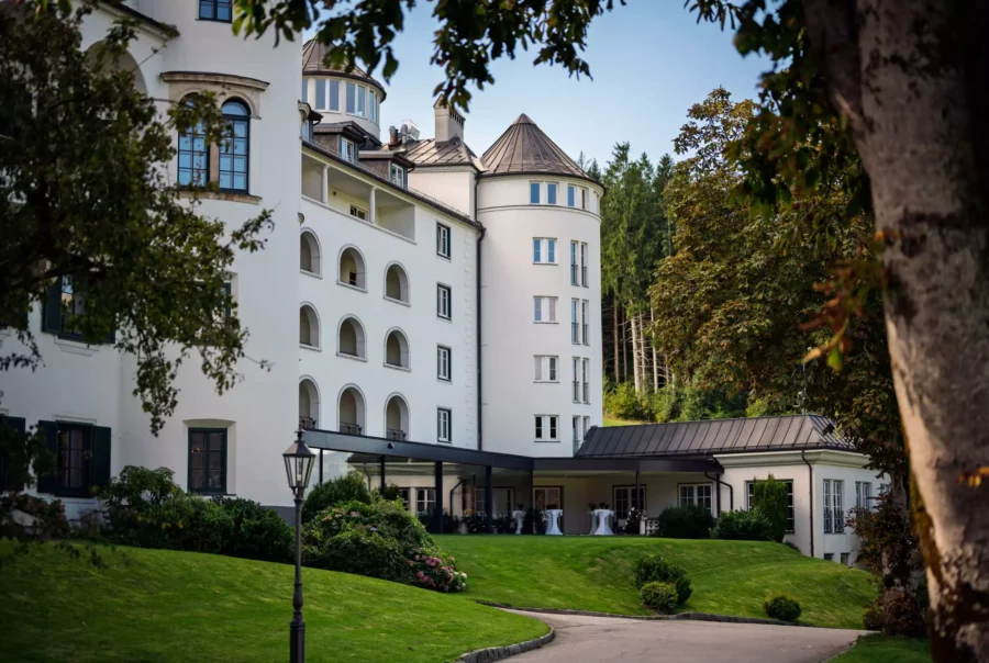 Weißes historisches Gebäude mit Rundturm, Arkaden und gepflegtem Garten in Pichlarn, umgeben von Bäumen und Wald im