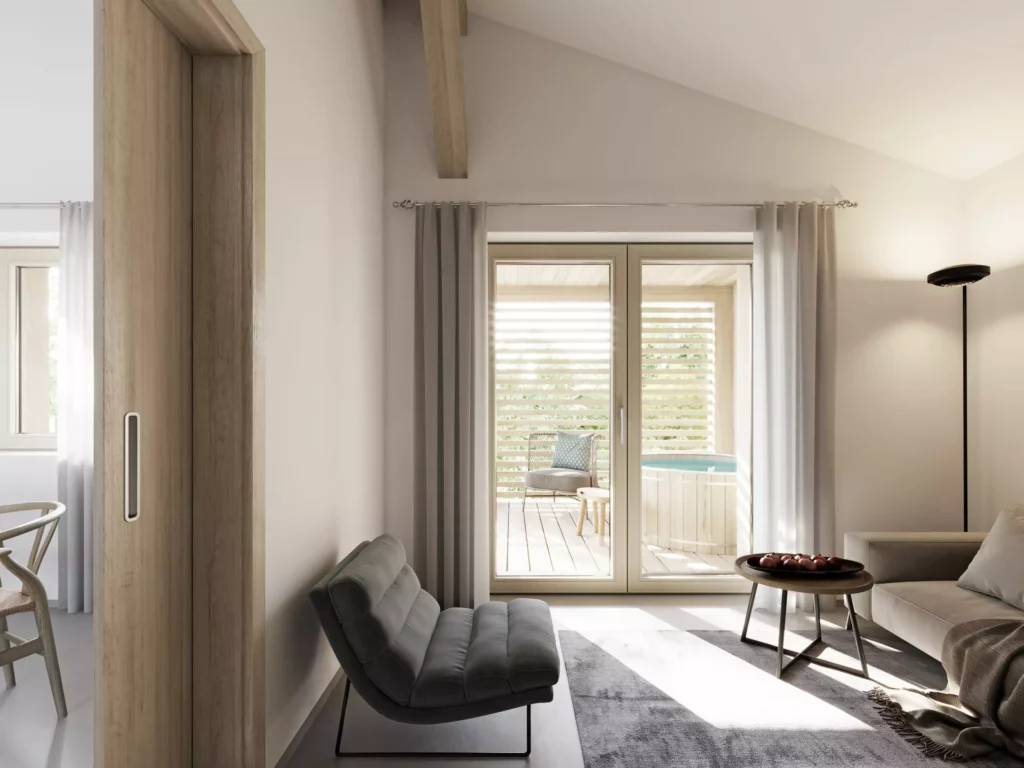 AppartementsNo37_2 Helles Wohnzimmer mit grauem Sessel, Sofa, runder Holzablage und Zugang zu Terrasse mit Stuhl und Whirlpool bei Tageslicht