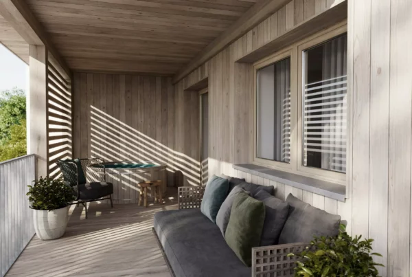 Überdachter Balkon mit Holzverkleidung, grauem Sofa, Stuhl, kleinem Tisch und Pflanzen, Sonnenlicht fällt durch Lamellen.