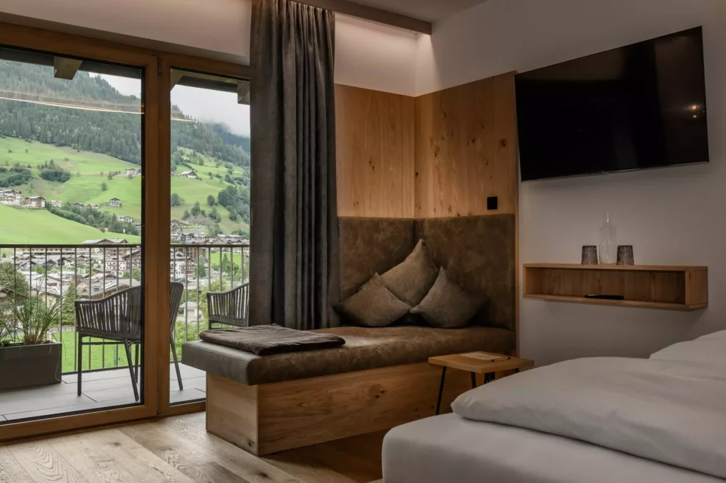 Hubertushof_07 Modern eingerichtetes Hotelzimmer mit Sitzbank, großem Fenster und Balkon mit Bergblick im Hubertushof