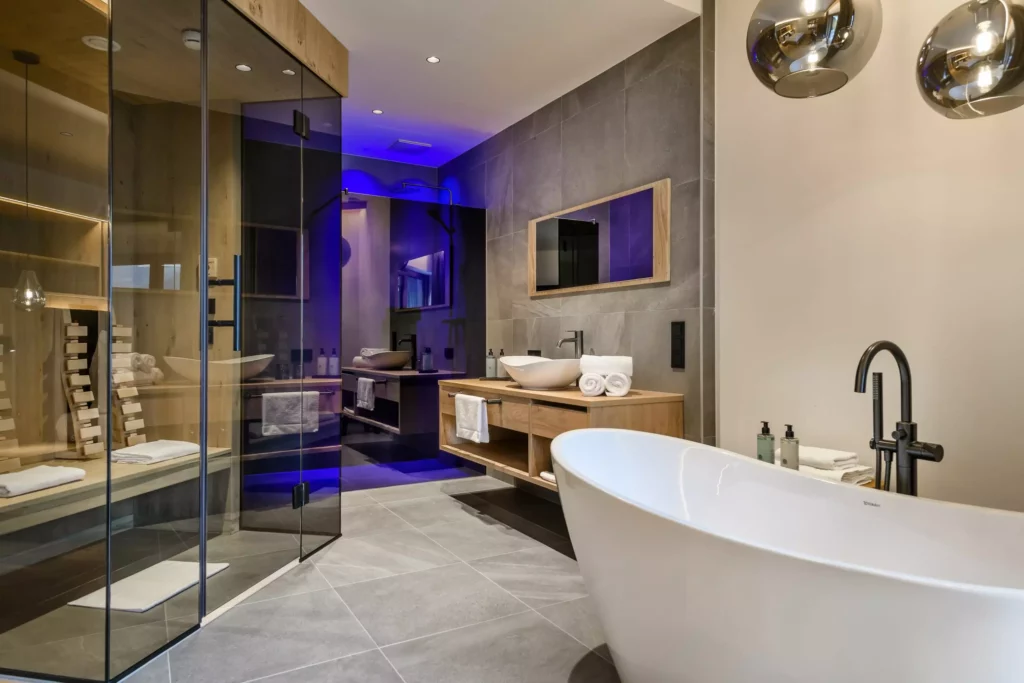 Hubertushof_08 Modernes Badezimmer mit freistehender Badewanne, Holzwaschtisch, Glasdusche und Sauna mit indirekter blauer Beleuchtung im