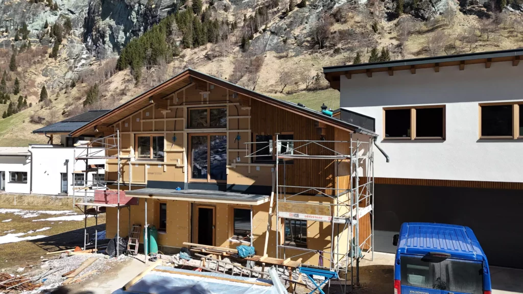 default Haus im Rohbau mit Gerüst und Baugeräten vor Bergkulisse im Hochbauprojektmanagement