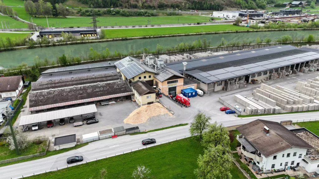 Thermospan Luftaufnahme eines Industriegebäudes mit Solarzellen auf dem Dach, Lagerflächen und Fahrzeugen, umgeben von Grünflächen und