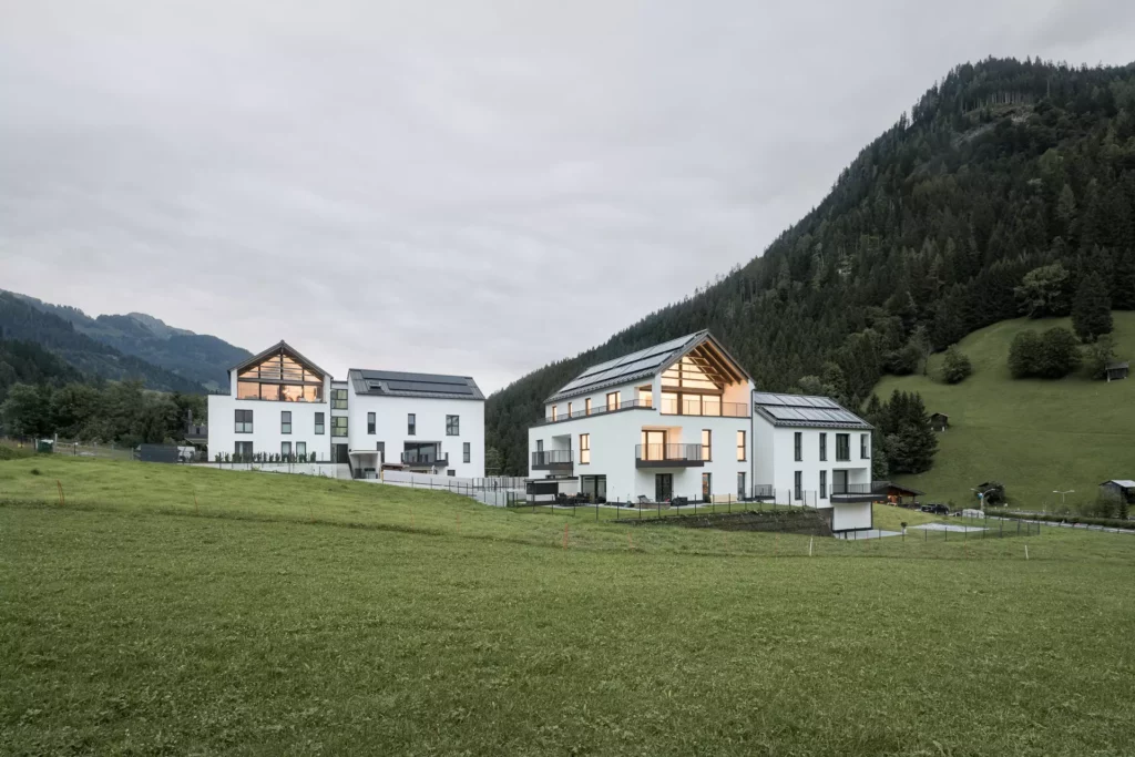 WB_Hofmann Moderne Wohngebäude mit großen Fenstern und Solarpanelen vor bewaldeten Bergen und grüner Wiese in Großarl