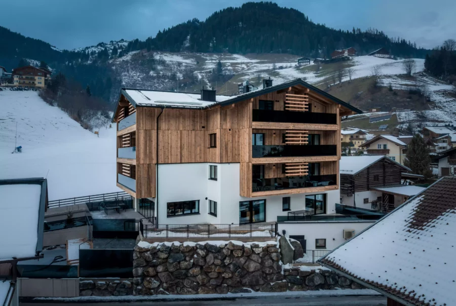 Modernes Holz- und Weißbauwerk in verschneiter Berglandschaft mit umliegenden Häusern und bewaldeten Hügeln bei Diellehen