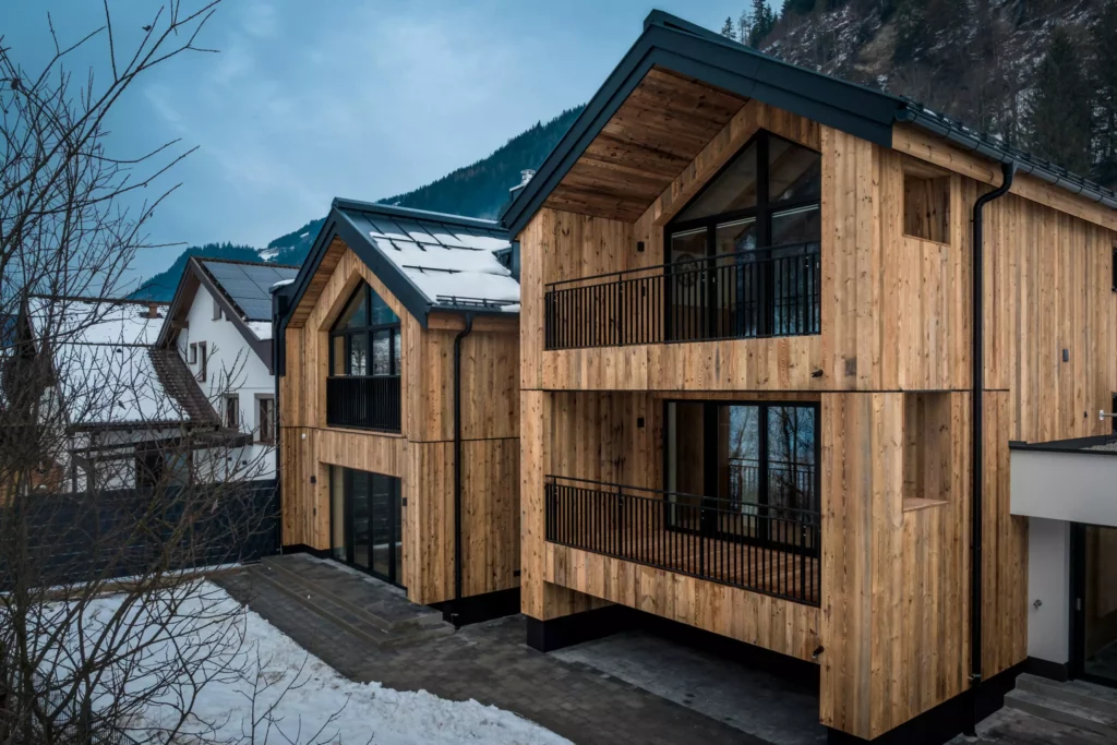 deutinger projektentwicklung baumanagement generalunternehmen immobilien grossarl hallein salzburg Hettegger-Sandra-©sobietzki-high-res-3 Modernes Holzhaus mit großen Fenstern und Balkonen in verschneiter Berglandschaft bei Dämmerung