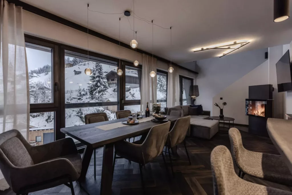 deutinger-projektentwicklung-baumanagement-generalunternehmen-immobilien-grossarl-hallein-salzburg-onkl-xonna-102-© Foto by studio manufaktur2 Modern eingerichteter Wohn- und Essbereich mit Kamin, großem Holztisch und Panoramafenstern mit Blick auf verschneite