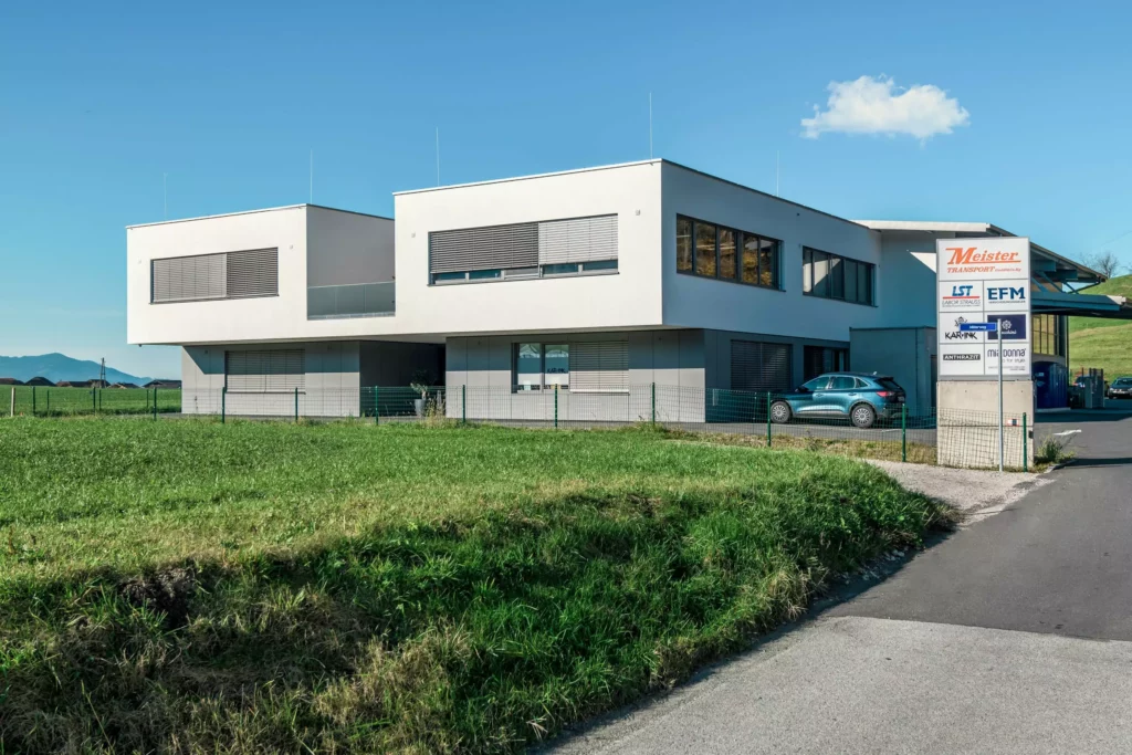 deutinger-projektentwicklung-baumanagement-generalunternehmen-immobilien-salzburg-Betriebshalle-Meister-Hallwang-1 Moderne Betriebshalle mit weißer Fassade und großen Fenstern in Hallwang bei Salzburg unter blauem Himmel