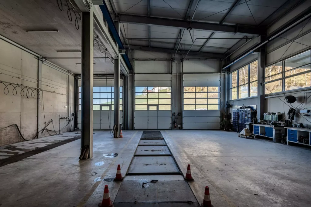 deutinger-projektentwicklung-baumanagement-generalunternehmen-immobilien-salzburg-Betriebshalle-Meister-Hallwang-10 Leere Betriebshalle mit großen Garagentoren, Werkbänken und Verkehrskegeln in Meister Hallwang bei Salzburg