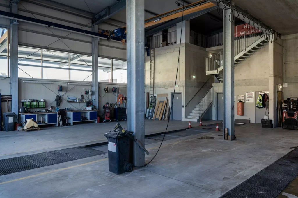 deutinger-projektentwicklung-baumanagement-generalunternehmen-immobilien-salzburg-Betriebshalle-Meister-Hallwang-13 Große Industriehalle mit Werkbänken, Treppe, Betonpfeilern und Arbeitsgeräten in einer Betriebshalle in Hallwang bei