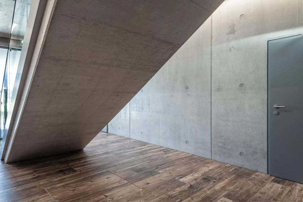 deutinger-projektentwicklung-baumanagement-generalunternehmen-immobilien-salzburg-Betriebshalle-Meister-Hallwang-22 Moderner Innenraum mit schräger Betontreppe, Sichtbetonwand und Holzoptik-Boden in einer Betriebshalle in Hallwang bei
