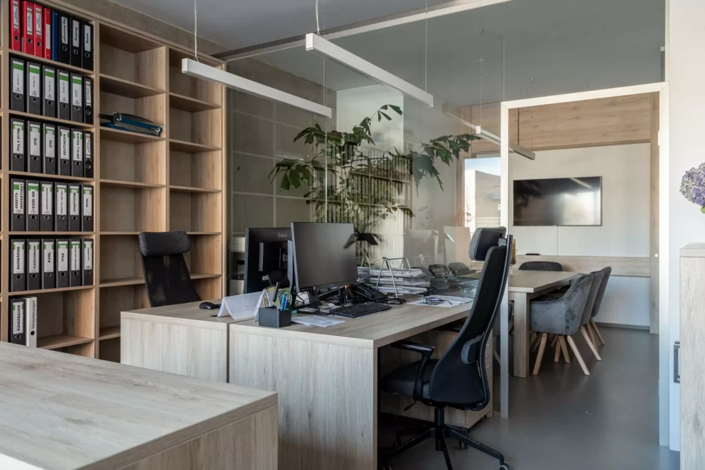 deutinger-projektentwicklung-baumanagement-generalunternehmen-immobilien-salzburg-Betriebshalle-Meister-Hallwang-23 Modernes Büro mit Schreibtischen, Computern, schwarzen Bürostühlen, Aktenregalen und einem Besprechungsraum mit Fernseher im
