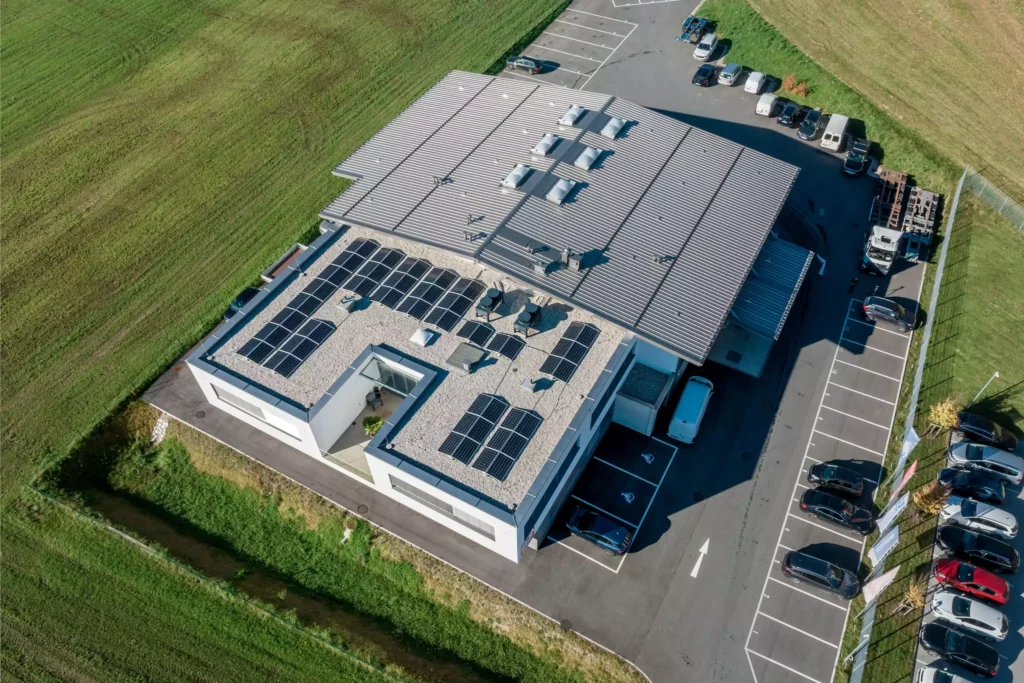 deutinger-projektentwicklung-baumanagement-generalunternehmen-immobilien-salzburg-Betriebshalle-Meister-Hallwang-8 Luftaufnahme einer modernen Betriebshalle mit Solarpaneelen auf dem Flachdach und angrenzendem Parkplatz in Hallwang bei