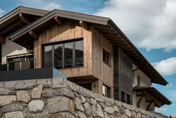 Modernes Mehrfamilienhaus mit Holzfassade und Natursteinmauer im Berggebiet bei Großarl unter blauem Himmel