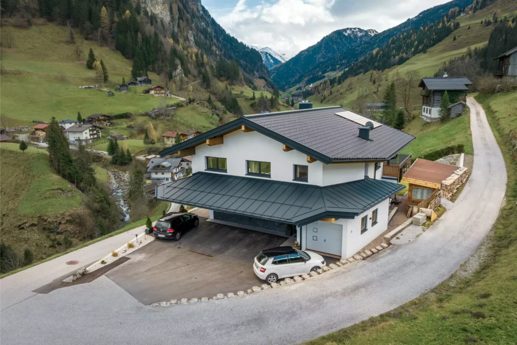 deutinger-projektentwicklung-baumanagement-generalunternehmen-immobilien-salzburg-MFH-Grossarl-Gfrerer-Schwarb-7 Modernes Mehrfamilienhaus mit Carport und zwei Autos in einem grünen Bergtal bei Großarl, Salzburg, umgeben von Bergen und