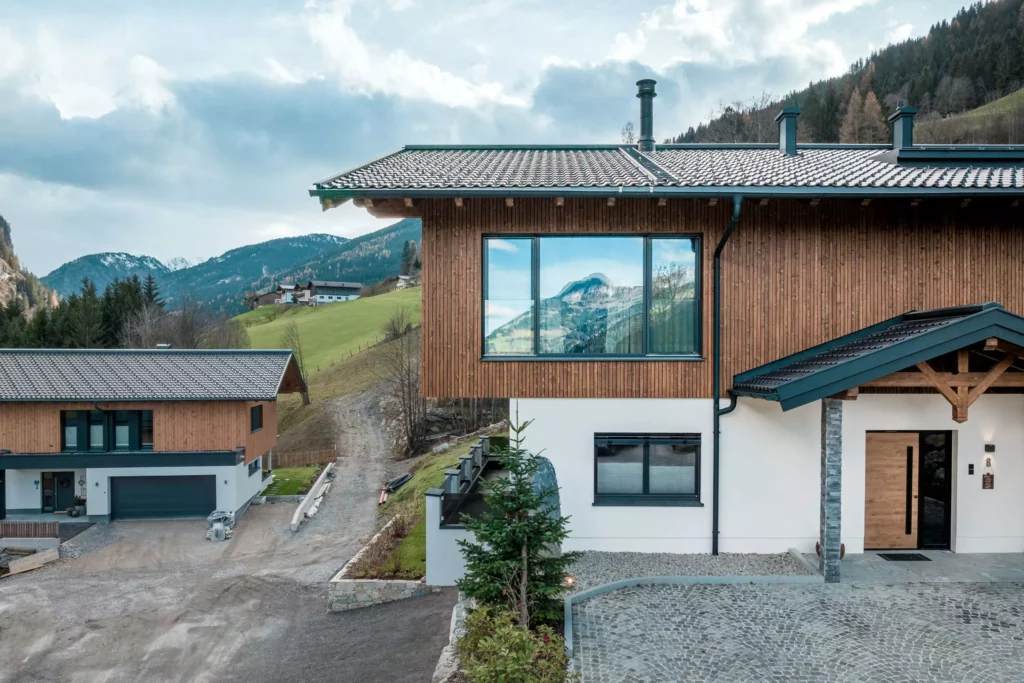 deutinger-projektentwicklung-baumanagement-generalunternehmen-immobilien-salzburg-MFH-Grossarl-Wagnermeyer-2 Modernes Mehrfamilienhaus mit Holzfassade und großen Fenstern in Großarl, umgeben von Bergen und grünen Wiesen