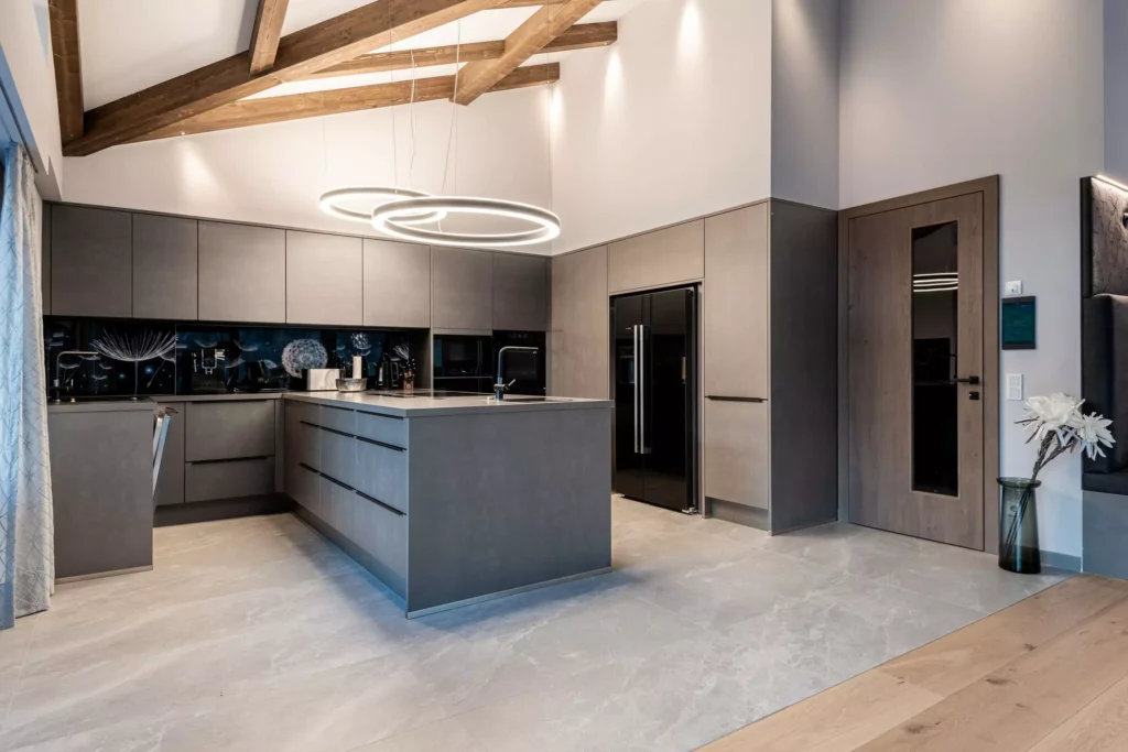 deutinger-projektentwicklung-baumanagement-generalunternehmen-immobilien-salzburg-MFH-Grossarl-Wagnermeyer-21 Moderne Küche mit grauen Fronten, Kücheninsel, schwarzen Geräten, Holzdecke mit sichtbaren Balken und runden LED-Hängelampen