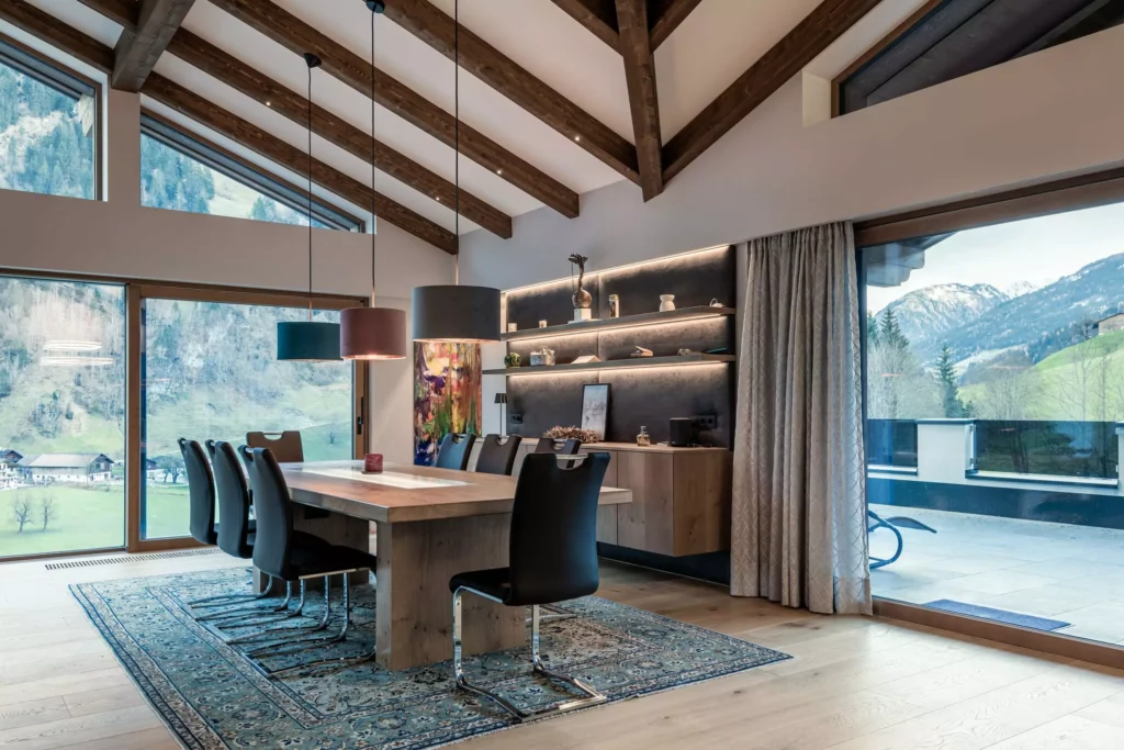 deutinger-projektentwicklung-baumanagement-generalunternehmen-immobilien-salzburg-MFH-Grossarl-Wagnermeyer-23 Moderner Essbereich mit Holztisch, schwarzen Stühlen, großen Fenstern und Bergblick in einem Mehrfamilienhaus in Großarl