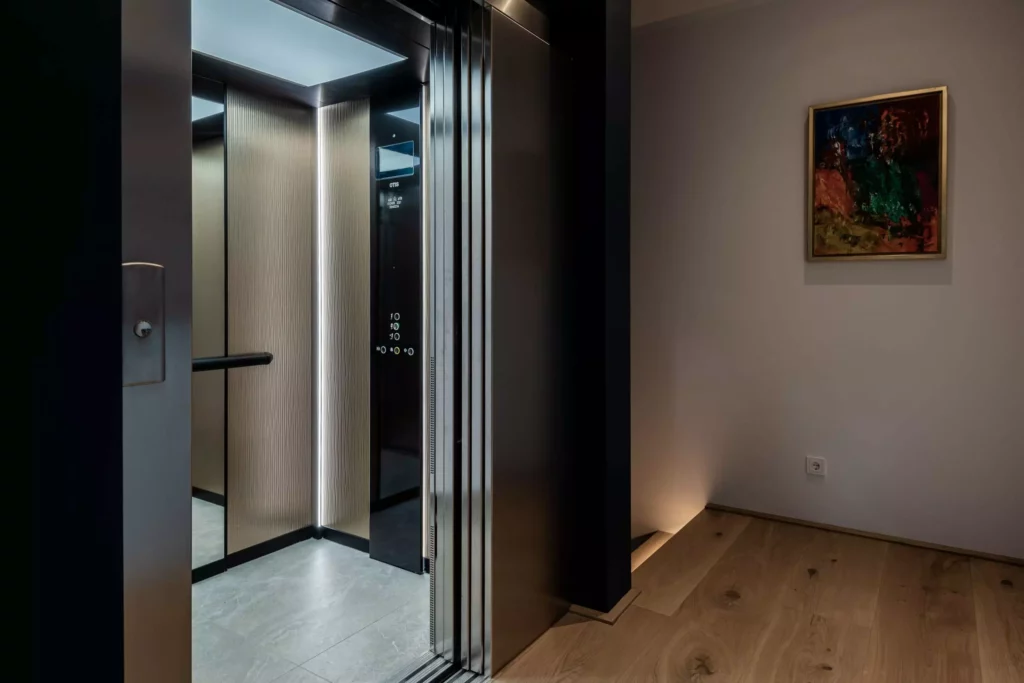 deutinger-projektentwicklung-baumanagement-generalunternehmen-immobilien-salzburg-MFH-Grossarl-Wagnermeyer-25 Moderner Aufzug mit geöffneter Tür in einem Wohngebäude mit Holzboden und abstraktem Bild an der Wand
