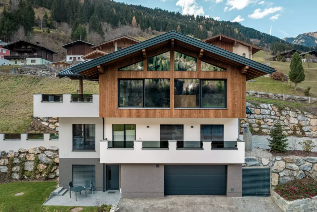 deutinger-projektentwicklung-baumanagement-generalunternehmen-immobilien-salzburg-MFH-Grossarl-Wagnermeyer-4 Modernes Mehrfamilienhaus mit Holzfassade und großen Fenstern vor bewaldetem Berghang in Großarl