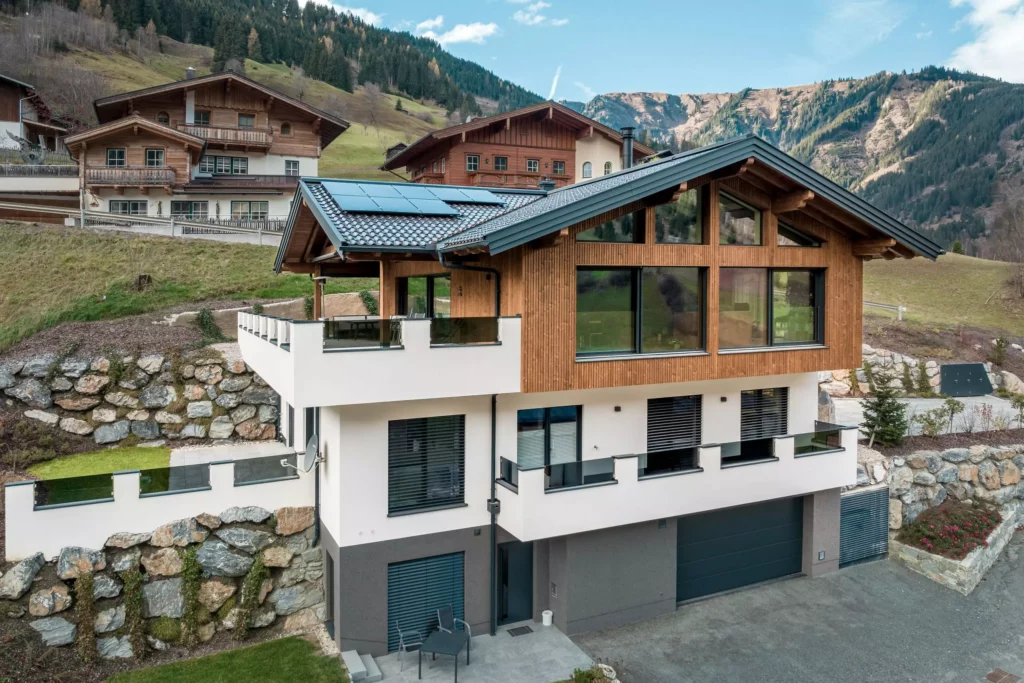 deutinger-projektentwicklung-baumanagement-generalunternehmen-immobilien-salzburg-MFH-Grossarl-Wagnermeyer-5 Modernes Mehrfamilienhaus mit Holzfassade und Solarpaneelen vor Bergkulisse in Großarl, Salzburg