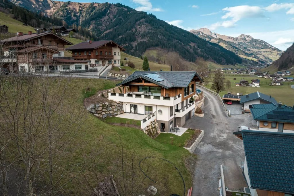 deutinger-projektentwicklung-baumanagement-generalunternehmen-immobilien-salzburg-MFH-Grossarl-Wagnermeyer-7 Modernes Mehrfamilienhaus mit Holzfassade und Solarpanelen in Großarl, eingebettet in alpine Berglandschaft mit Straßen und