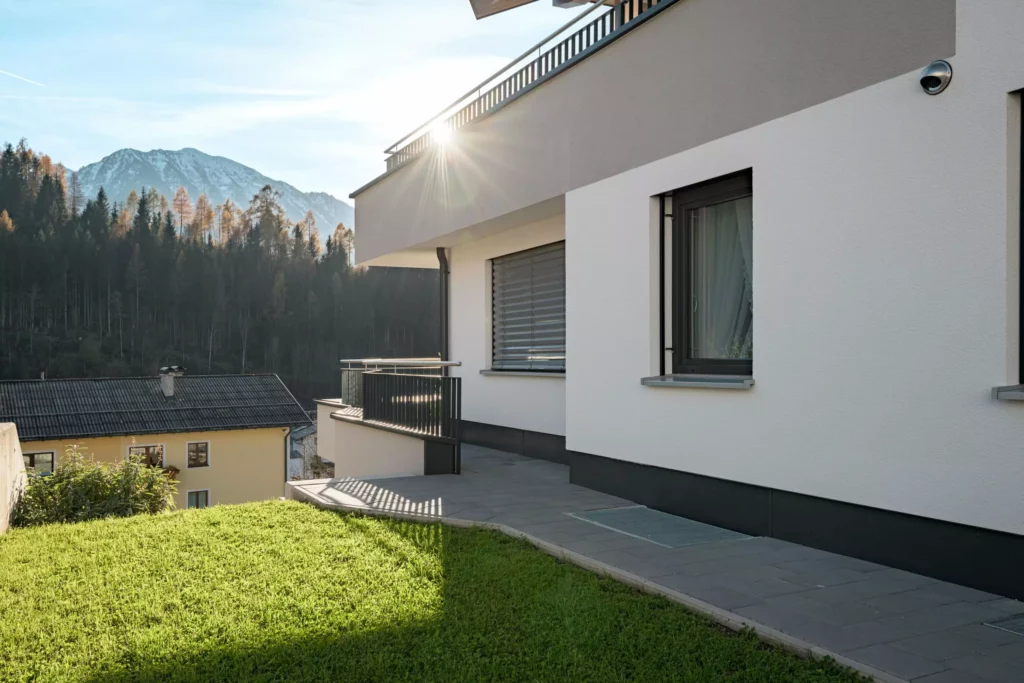 deutinger-projektentwicklung-baumanagement-generalunternehmen-immobilien-salzburg-Mehrfamilienhaus-Altenberger-2 Modernes Mehrfamilienhaus mit Terrasse und Bergpanorama in Salzburg bei Sonnenuntergang, gepflegter Gartenbereich sichtbar