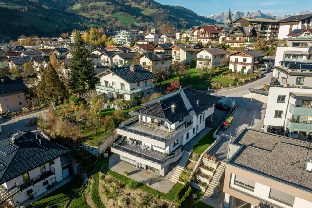 deutinger-projektentwicklung-baumanagement-generalunternehmen-immobilien-salzburg-Mehrfamilienhaus-Altenberger-5 Modernes Mehrfamilienhaus mit großen Balkonen in einer Wohnsiedlung vor Bergkulisse bei klarem Himmel