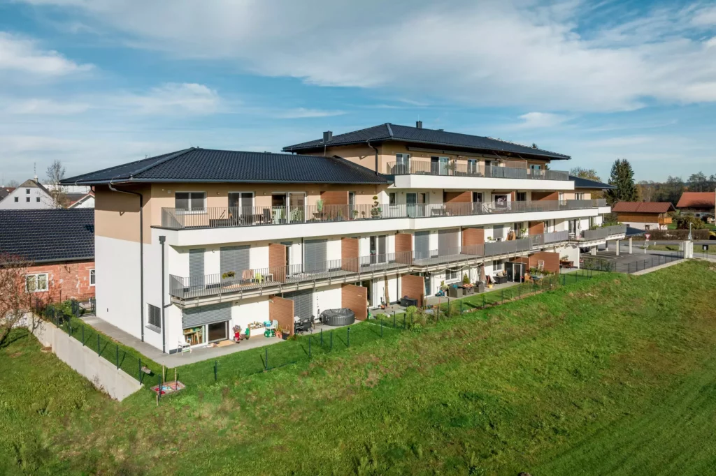 deutinger-projektentwicklung-baumanagement-generalunternehmen-immobilien-salzburg-Panoramapark-Uttendorf-10 Modernes Wohngebäude mit Balkonen und Gartenflächen im Panoramapark Uttendorf bei Salzburg unter blauem Himmel
