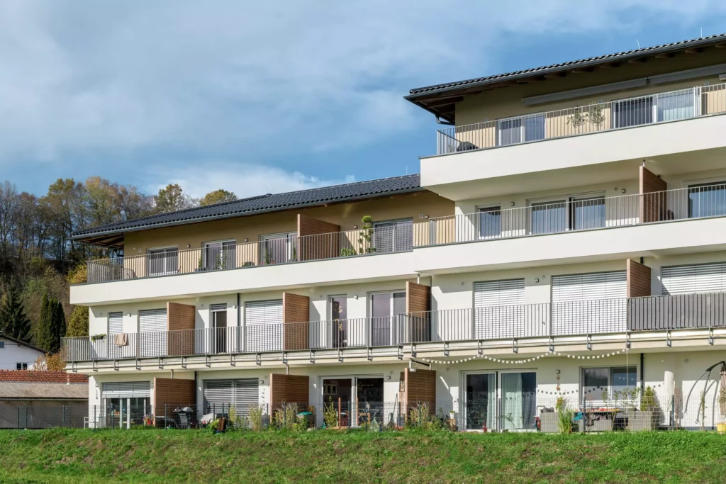 deutinger-projektentwicklung-baumanagement-generalunternehmen-immobilien-salzburg-Panoramapark-Uttendorf-2 Modernes Wohngebäude mit Balkonen und großen Fenstern vor bewaldetem Hügel und blauem Himmel in Uttendorf Salzburg