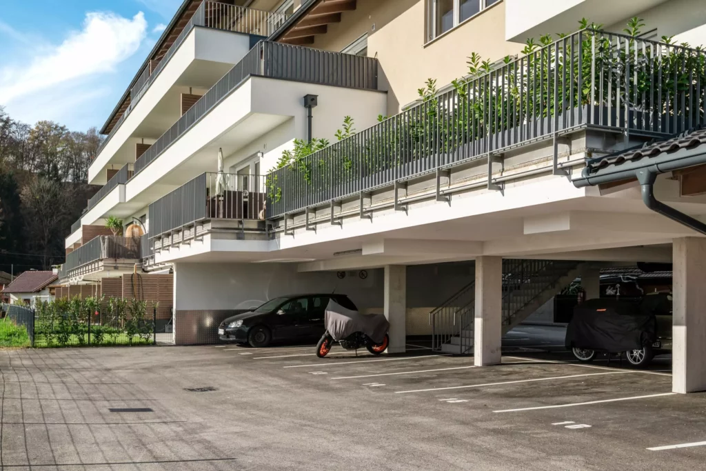 deutinger-projektentwicklung-baumanagement-generalunternehmen-immobilien-salzburg-Panoramapark-Uttendorf-3 Moderner Wohnkomplex mit überdachten Parkplätzen und Balkonen mit Metallgeländern in Uttendorf Salzburg Panoramapark
