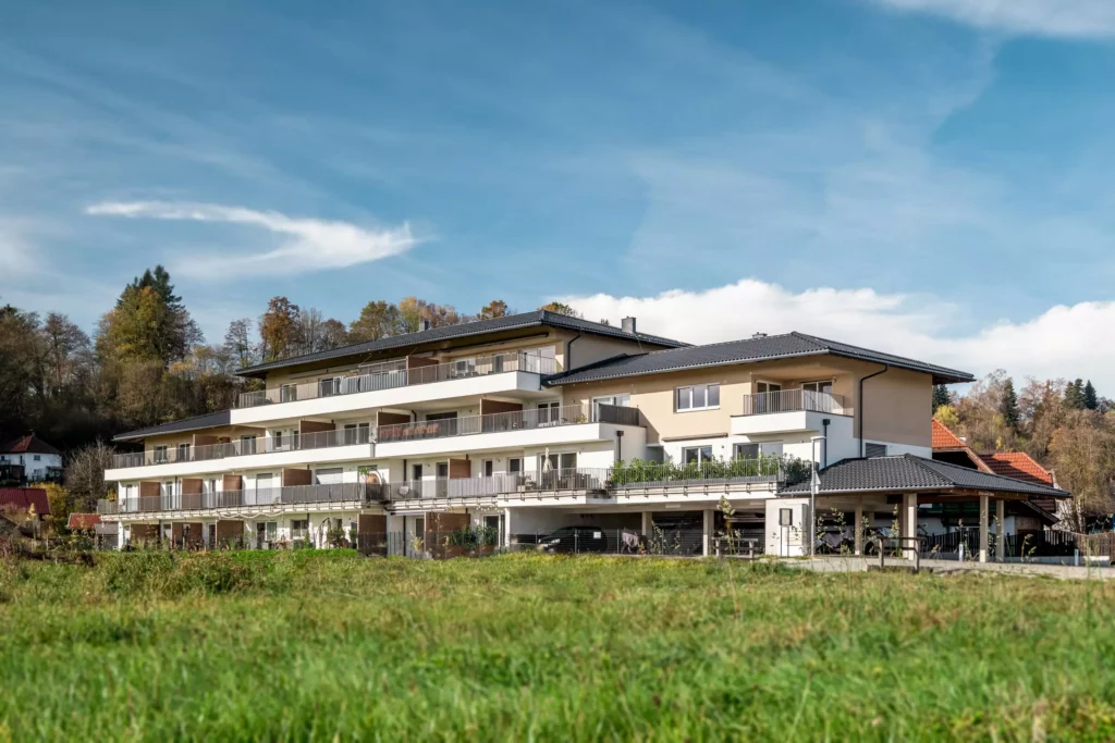 deutinger-projektentwicklung-baumanagement-generalunternehmen-immobilien-salzburg-Panoramapark-Uttendorf-5 Modernes Wohngebäude mit großen Balkonen vor herbstlichem Wald und grünem Feld im Panoramapark Uttendorf Salzburg